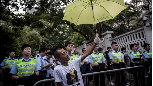 2014年10月22日，香港金钟抗议地点游行后，一名民主抗议者在守卫总督府的警察前撑着雨伞。