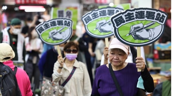 游盈隆認為，若無民進黨介入大罷免行動，無法成就今日局面。圖為民進黨參與志工拿著「民主連署站」手舉牌在市場內宣傳。（圖片來源：中央社）