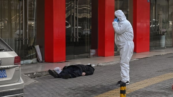 2020年1月30日，在武汉一家医院附近的街道上，一名身穿防护服的工作人员正在查看一名倒地身亡的老人。（图片来源：HECTOR RETAMAL/AFP via Getty Images）