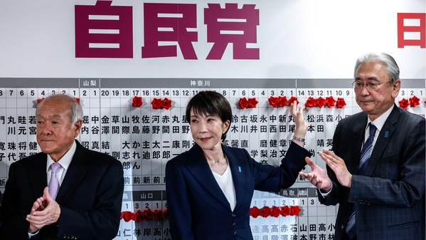 2026年2月8日，在东京举行的众议院选举期间，日本首相兼自民党总裁高市早苗（中）站在自民党干事长铃木俊一（左）和自民党选举策略会长古屋敬二身旁，在自民党总部将一朵红纸玫瑰放在一位当选候选人的名字上。（Kim Kyung-Hoon/POOL/AFP via Getty Images)